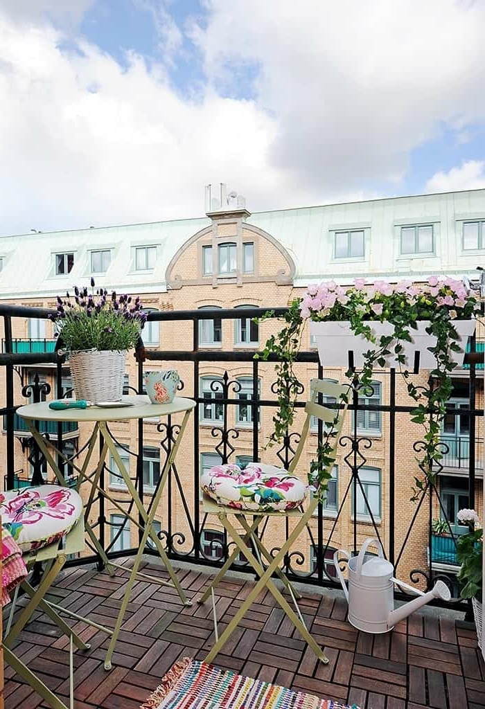 Balkon Lounge Klein, Design mit Blumen und Kissen mit Blumenmotiven, bunter Teppich, weiße Gießkanne