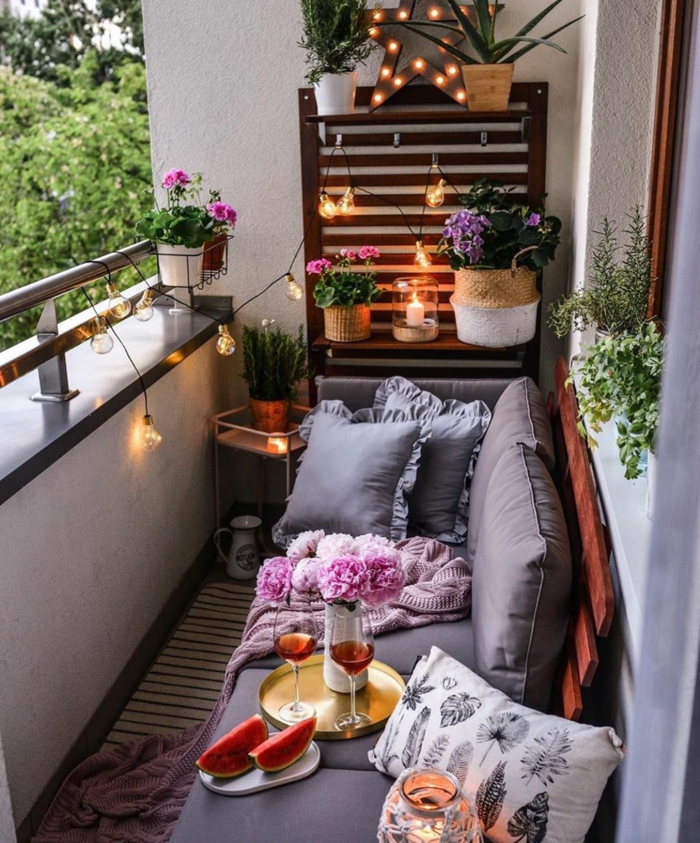 Balkonmöbel set für kleinen Balkon, Sofa mit grauen Kissen, Tablett mit Wein und Wassermelone, Pflanzen und Blumen