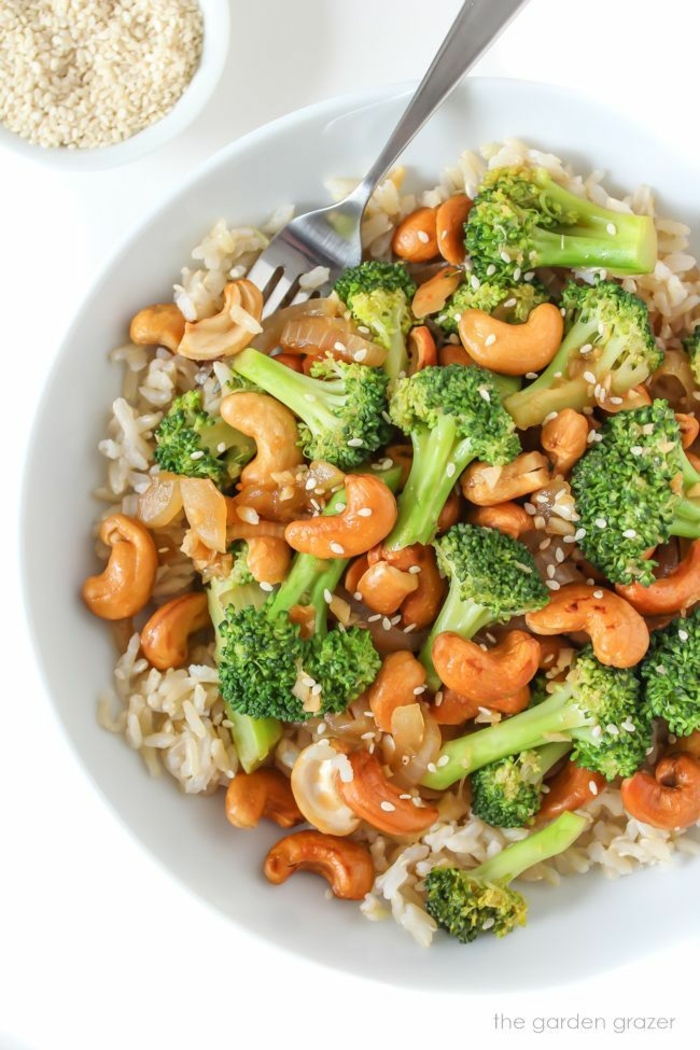 leckere Gemüse Rezepte vegan, Reis mit Brokkoli und gerösteten Cashewkernen in einer weißen Schale mit Gabel