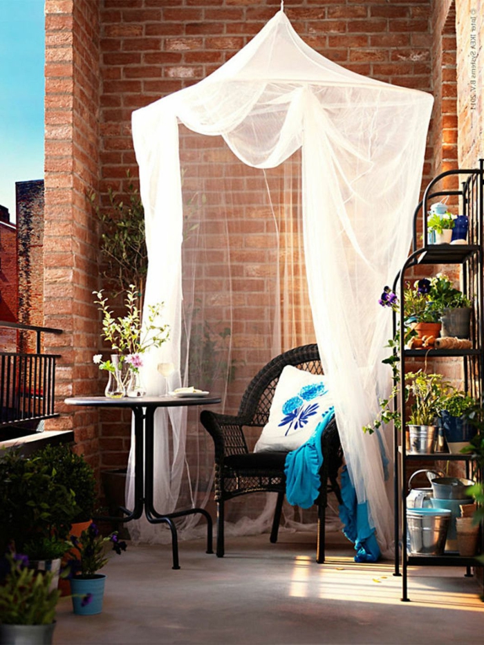 Balkon gestalten Ideen, Design mit weißem Baldachin, weißer Kissen mit blauen Motiven, großer Pflanzenständer