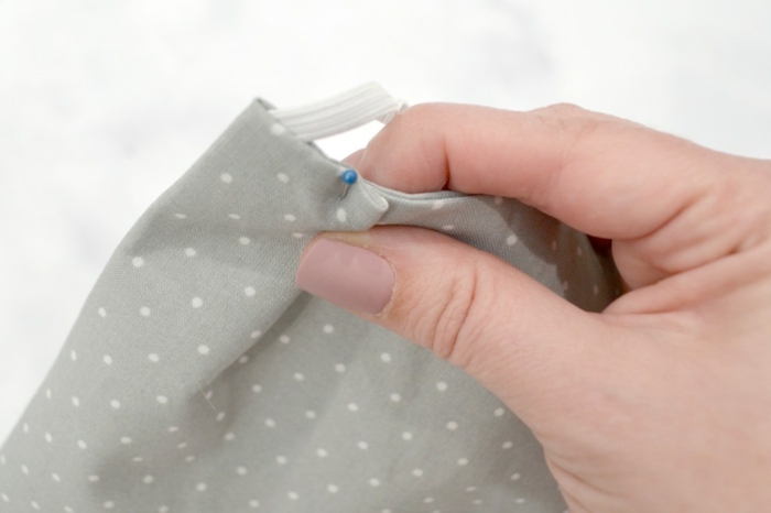 Hand hält Stoff mit einer Stecknadel, Atemschutzmaske selber machen, DIY Anleitung