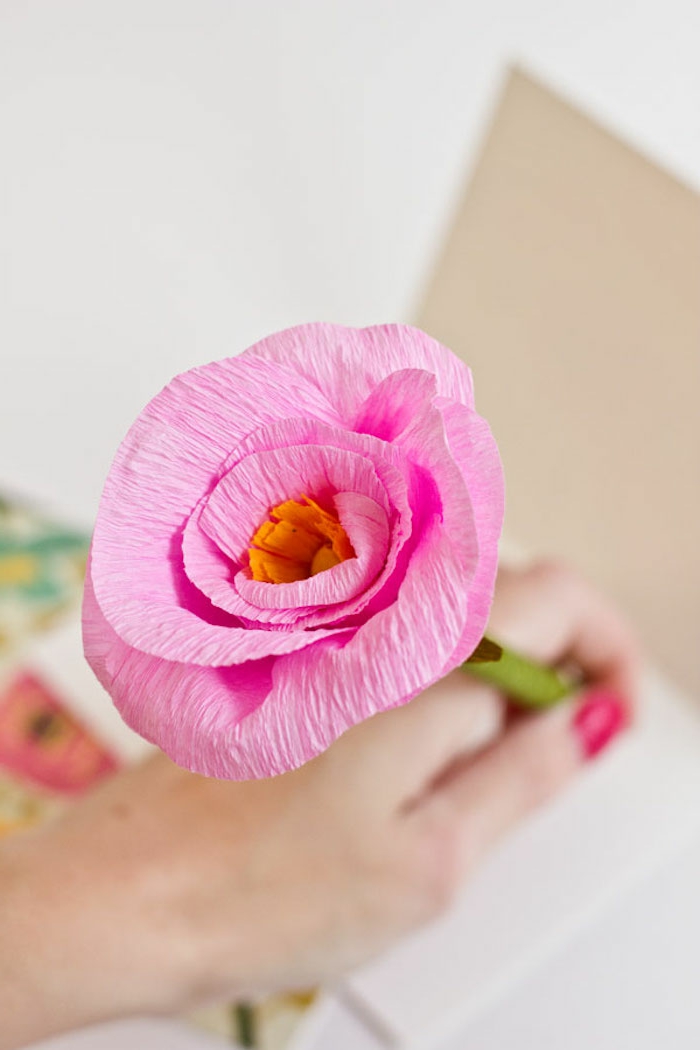 Deko Ideen selbermachen Frühling, pinke Blume aus Krepppapier, Hand hält einen Stift