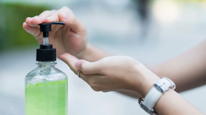 eine flasche mit einem grünen desinfektionsmittel gegen viren, eine hand mit ring und einer weißen uhr, desinfektionsmittel selber machen 