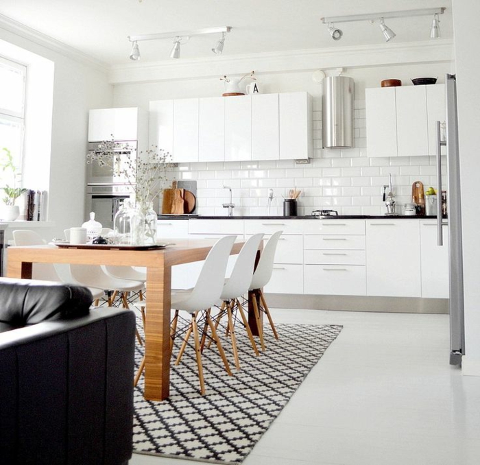 großer Esstisch aus Holz mit weißen Stühlen, schwarz weißer Teppich, monochrome weiße Küchenschränke, Couch aus Leder in schwarz, designer Küchen