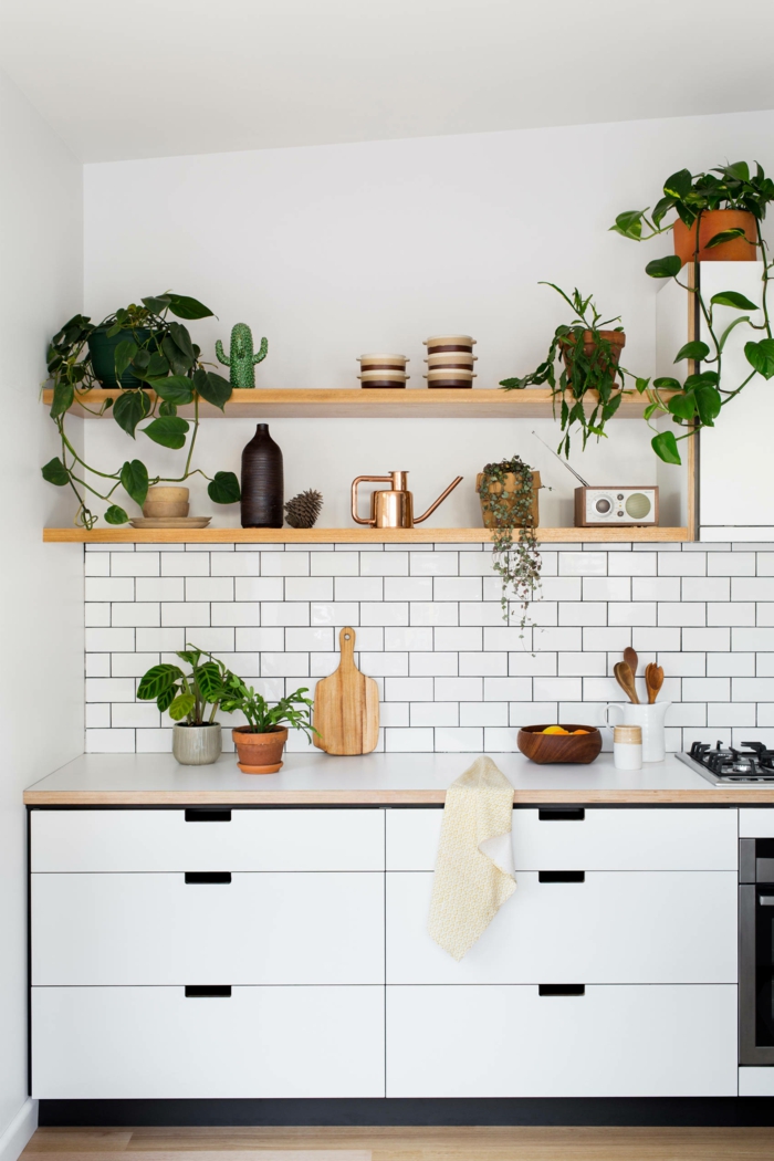 Küche dekorieren Tipps, weiße Fliesen und Schränke, Regale mit grünen Pflanzen und Küchenutensilien