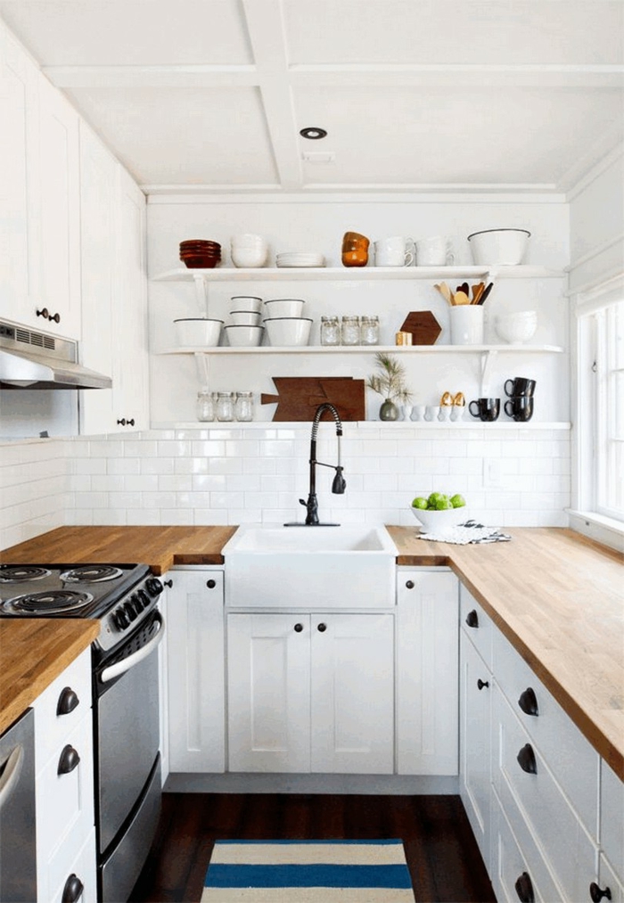 Kleine Küche u Form mit Fenster, weiß blauer Teppich, Arbeitsplatte aus Holz, Tassen und Teller auf einem Regal