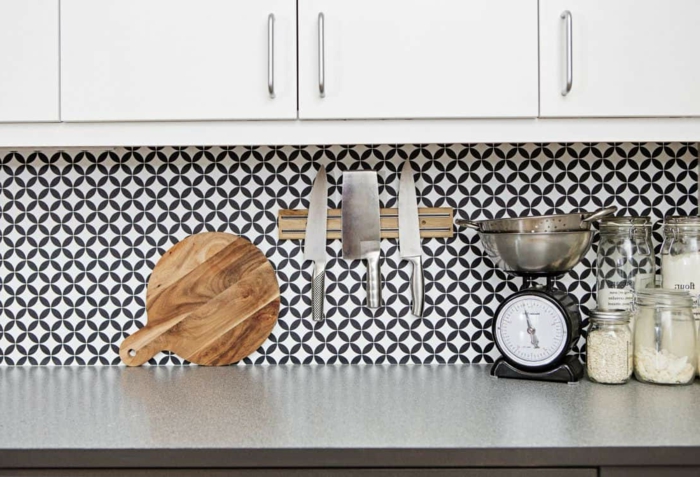 Wandgestaltung Küche mit schwarz weißer Tapete, Schneidebrett aus Holz, drei große Messer, weiße Küchenschränke