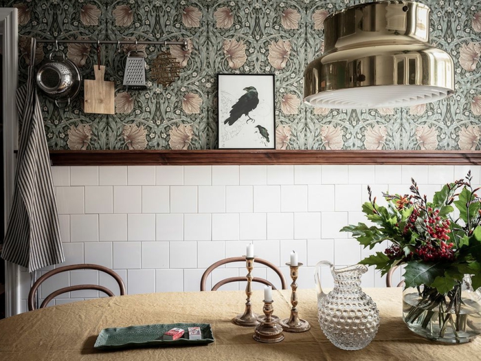 weiße Fliesen, Küchen Tapeten grün mit Blumenmotiven, Bild von einer schwarzen Rabe, Blumen in Vase, aufgehängte Küchenutensilien