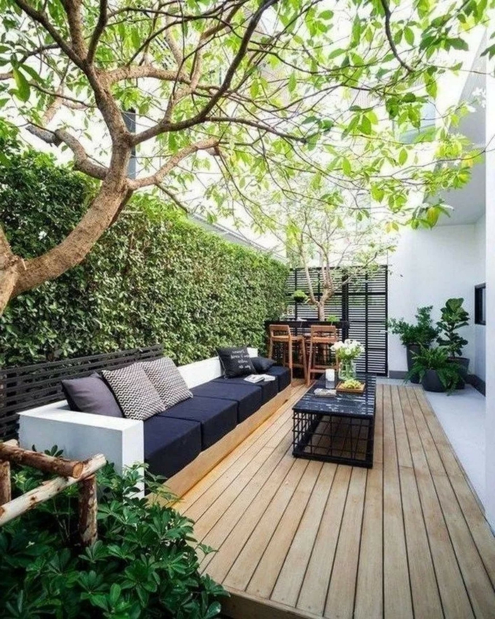 Gartengestaltung Sichtschutz Beispiele mit Pflanzen, minimalistische Einrichtung von Terrasse mit schwarzem Sofa, Boden aus Holz,