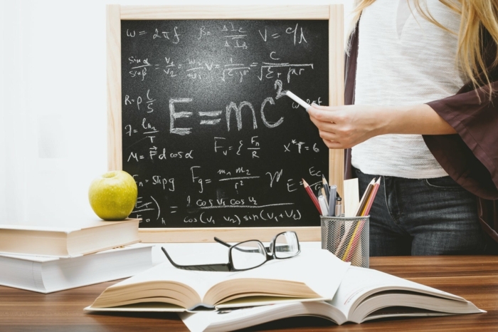 schwarze Tafel mit Gleichungen, viele Bücher auf dem Tisch, Weiterbildung nach Ausbildung, grüner Apfel, schwarze Brillen