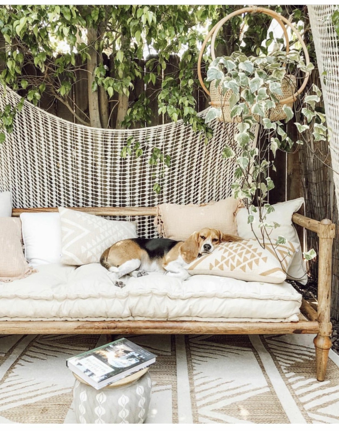 Hund liegt auf einem Sofa aus Bambus mit weißer Polsterung, Garten Trennwand Holz, Sichtschutz mit Zaun und Baum