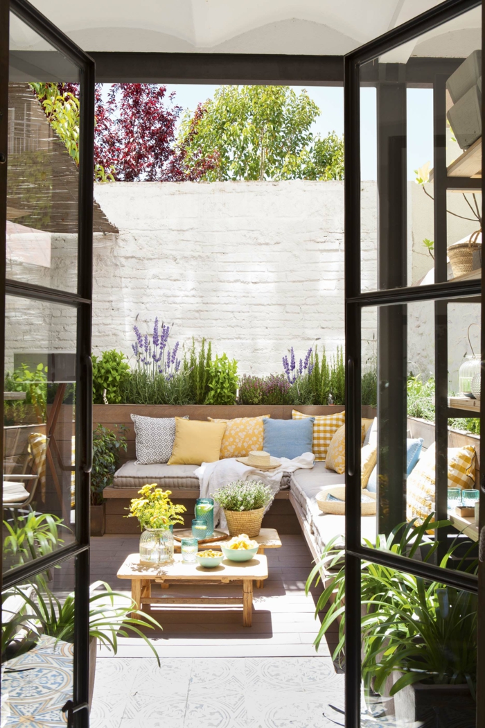 Sichtschutz Terrasse modern, großer weißer Gartenzaun, Ecksofa mit gelben und blauen Kissen, Dekoration mit vielen Pflanzen