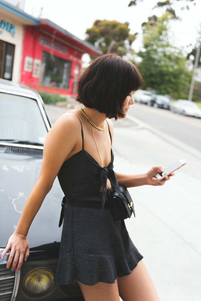 Schwarzes Sommerkleid, Outfit Inspiration, kleine Tasche, Bob Frisuren kurz stufig, Frau guckt auf ihr Handy