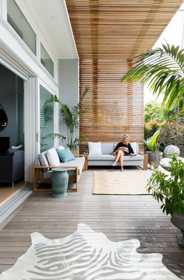Terrassengestaltung mit Sichtschutz, luxuriöse Außeneinrichtung mit Gartenzaun aus Holz, junge Frau sitzt auf einem Sofa,