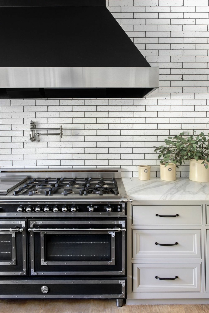 Abwaschbare Tapete Küche mit Flieseneffekt, weiße Schränke und schwarzer Offen, Dekoration mit Pflanze