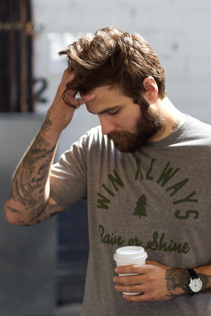 Männer Frisuren Kurz 2020 Trend, Mann mit vielen Tattoos auf dem Arm, hält eine weiße Tasse Kaffee, angezogen im grauen T-Shirt