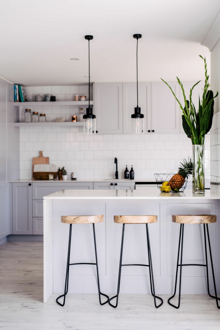 kleine moderne Küche mit Kochinsel, monochrome Einrichtung in weiß, zwei schlichte Hängelampen, Vase mit grünen Pflanzen
