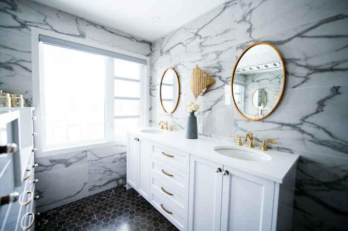 Zwei runde Spiegel mit goldenen Rahmen, weiße Schränke, Wände mit Marmor-Effekt, Badspiegel nach Maß, schwarze Bodenfliesen