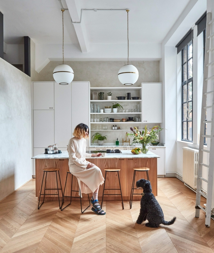 elegante Frau sitzt auf einem Stuhl in ihrer Küche, schwarzer Hund, Kücheninsel mit Sitzgelegenheit, großes französisches Fenster 