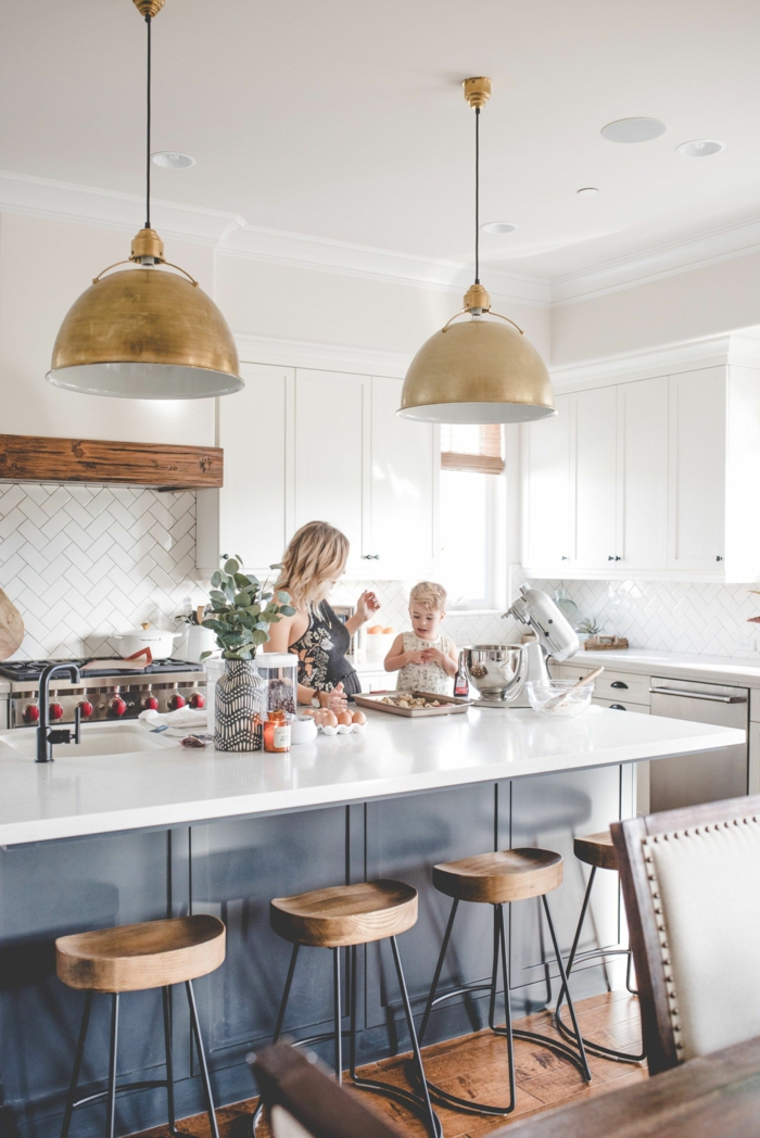 Mutter und kleines Kind kochen zusammen, blaue Kochinsel mit Theke in weiß, zwei goldene Hängelampen, Küchenschränke weiß