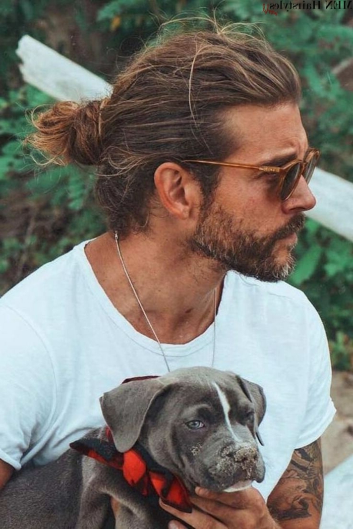 Haarschnitt lange Haare 2020, Mann mit dunkelblonden Haare im Man Bun, Herr trägt ein weißes T-Shirt, hält einen kleinen dunkelgrauen Hund