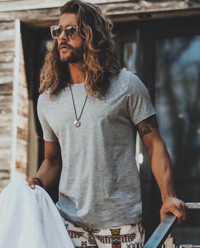 Haarschnitt lange Haare, Männerfrisuren 2020, lässig angezogener Mann in grauem T-Shirt und bunten Hosen