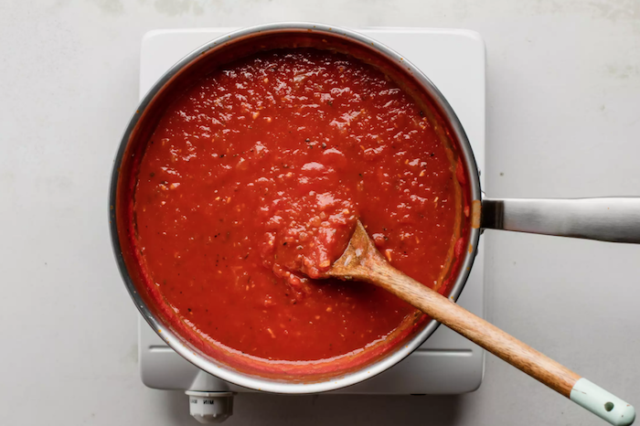 ein löffel aus holz und ein topf mit einer eigekochten diy frischen tomatensoße eine herdplatte tomaten einkochen