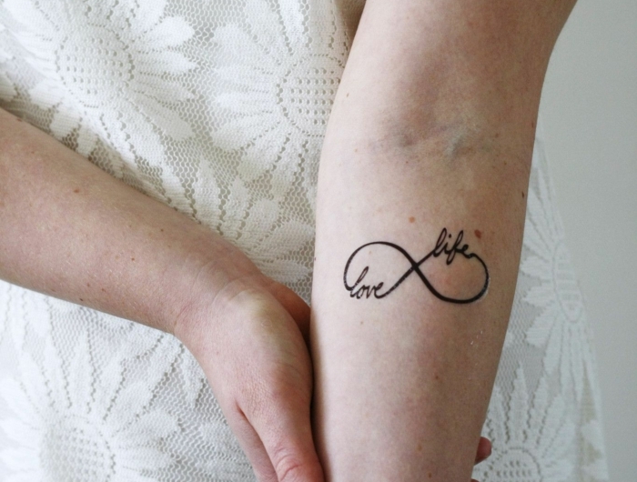 love life mini tattoo mit bedeutung unendlichkeitssymbol frau im weißen kleid mit blumen