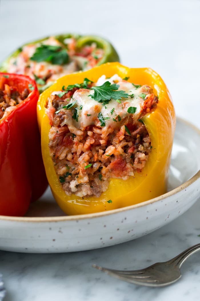 wie kocht man gefüllte paprika tomatensoße ein weißer teller mit gelben grünen und roten paprikaschoten und basmatireis