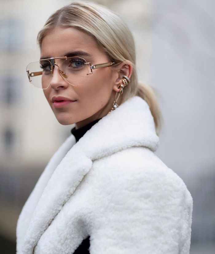 caro daur street style inspiration kurze blonde haare niedriger zopf verschiedene ohrringe brillenmode 2020 damen weißer flauschiger mantel