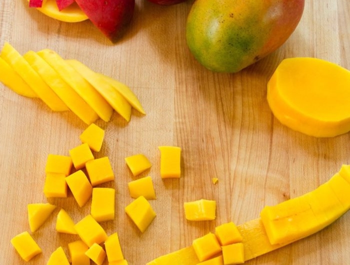 ein holzbrett mit messer und mango in vielen kleinen gelben scheiben grüne und rote mango schale