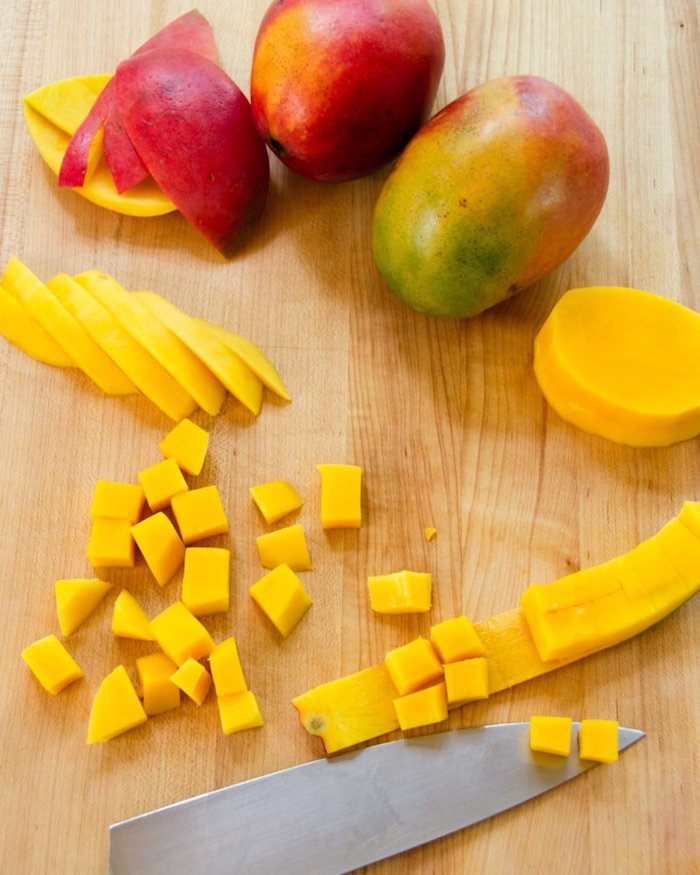 ein holzbrett mit messer und mango in vielen kleinen gelben scheiben grüne und rote mango schale