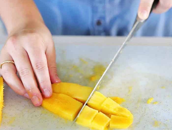 frau mit blauem hemd ein messer und gelbe geschnittene scheiben aus mango
