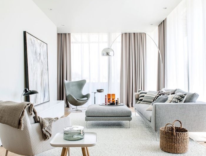 modernes skandinavisches wohnzimmer beige und graue farbtöne holzakzente große fenster mit gardinen großes gemälde an der wand skandi teppich