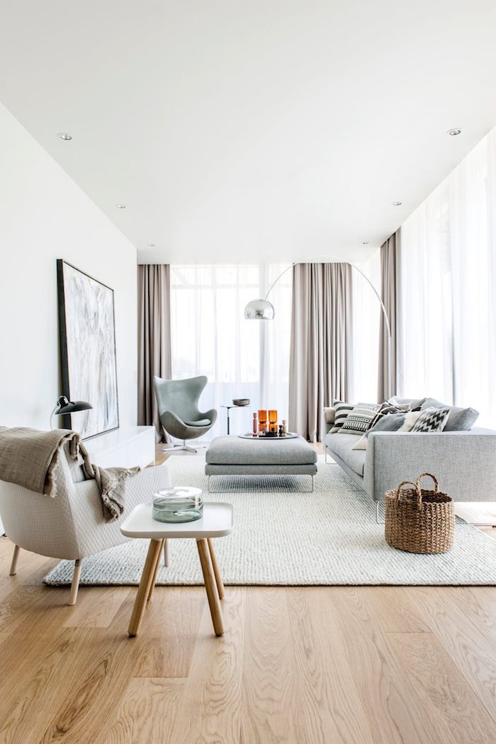 modernes skandinavisches wohnzimmer beige und graue farbtöne holzakzente große fenster mit gardinen großes gemälde an der wand skandi teppich