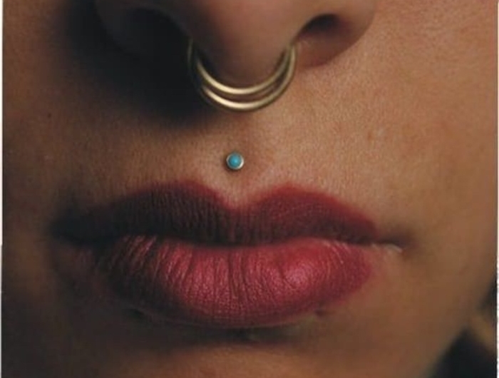 nahaufnahme roter lippenstift nasenringe und oberlippenpiercing mit blauem stein inspiration für medusa piercing tattoos am körper