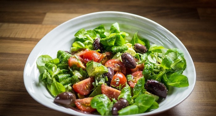 ein weißer teller mit grünen blättern eines feldsalats und schwarzen oliven und tomaten feldsalat rezepte