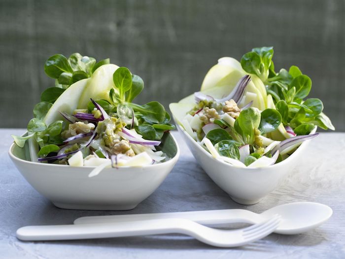 löffel und gabel aus plastik zwei weiße schüssel mit salaten mit grünen blättern eines feldsalats dressing für feldsalat