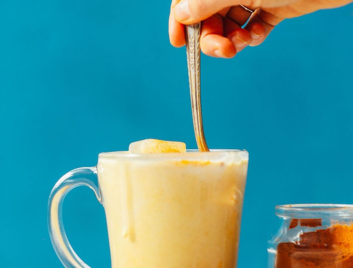 vegane goldene milch rezept ein glas mit gelber milch eine hand mit löffe ein glas mit kurkuma