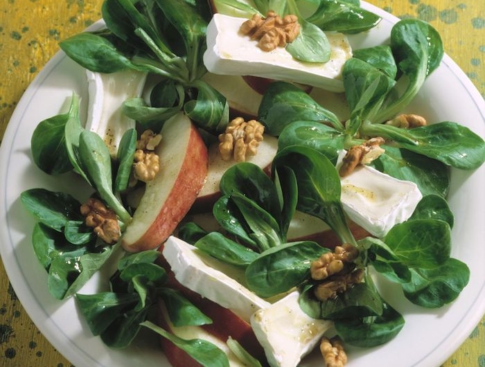 weißer teller mit salat mit frischen walnüssen geschnittenen äpfeln und grünen blättern eines feldsalats