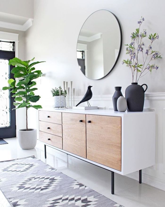 5 minimalistische inneneinrichtung weiße kommode türe aus holz geometrischer teppich skandinavische deko figuren schwarzer vogel vasen weißer topf grüne pflanze runder spiegel