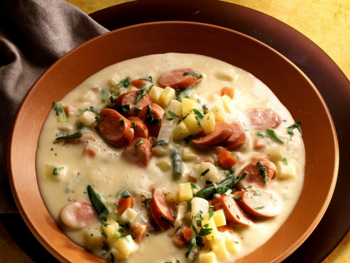 braune schüssel mit einer suppe mit kartoffeln und würstchen und speck