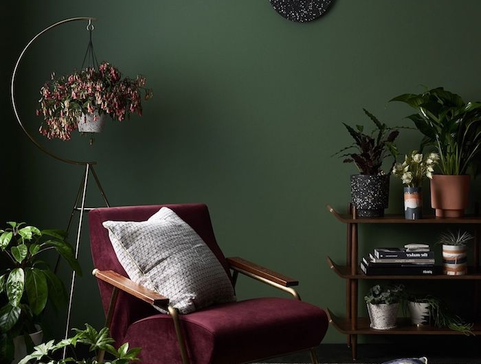 burgundfarbener stuhl weißes kissen wandfarbe grün deko wohnzimmer modern viele pflanzen und blumen schwarze runde wanduhr moderne inneneinrichtung
