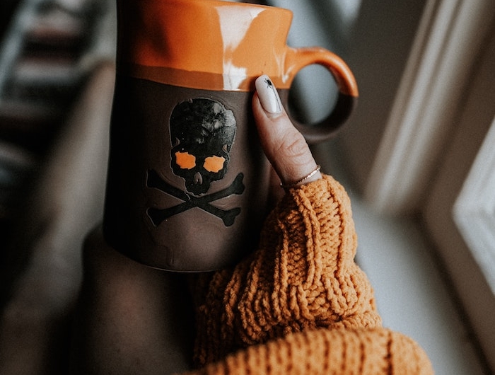 eine halloween tasse mit einem großen schwarzen totenkopf fenster eine frau mit hand mit einem orangen nagellack