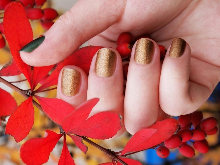 eine hand einer frau nageldesign herbst ein goldener nagellack herbst ein ast mit kleinen roten blättern