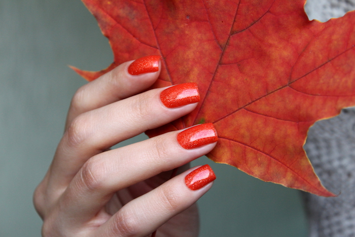 großes rotes blatt eine hand mit roten fingernägeln eine frau mit rotem nagellack