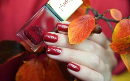 hand einer frau mit nagellack mit rotnuancen ein ast mit orangen und gelben blätter im herbst nagellack