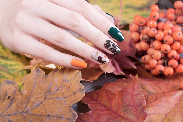 ideen für nageldesign herbst eine hand mit orangem und dunkelgrünem nagellack große orange und rote blätter