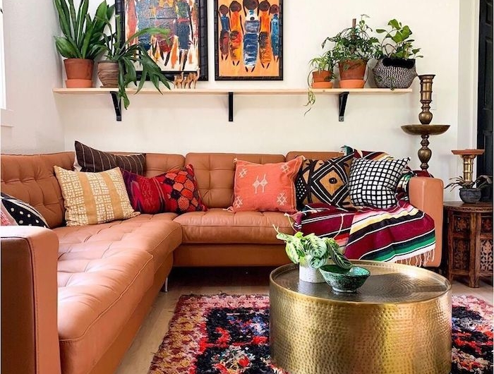 moderne dekoartikel stilvolle deko wohnzimmer modern einrichten boho chic inneneinrichtung ecksofa aus leder runder goldener kaffeetisch bunter teppich abstrakte bilder grüne pflanzen