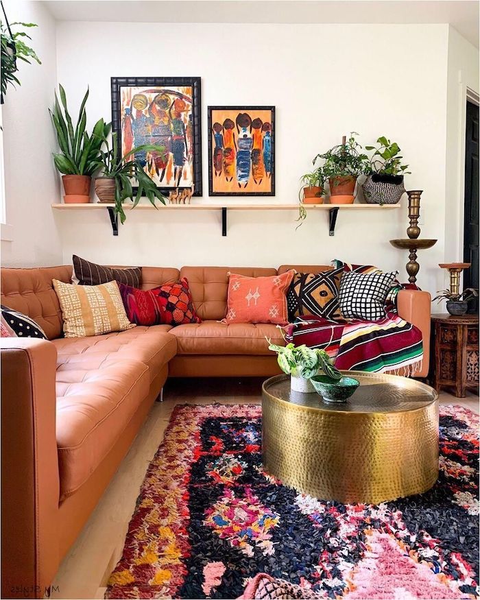 moderne dekoartikel stilvolle deko wohnzimmer modern einrichten boho chic inneneinrichtung ecksofa aus leder runder goldener kaffeetisch bunter teppich abstrakte bilder grüne pflanzen